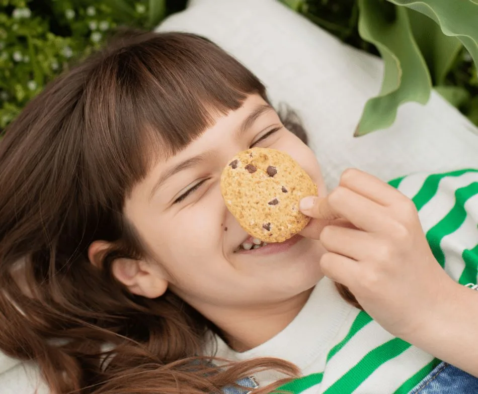 Niña tumbada sonriendo con Cookie de Avellanas y Chips de Chocolate de Milola Gluten-Free