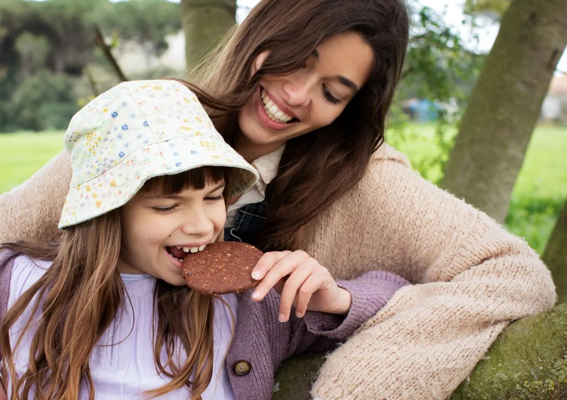 madre-e-hija-apoyadas-en-arbol-comiendo-galleta-vegana-de-chocolate-de-milola-gluten-free