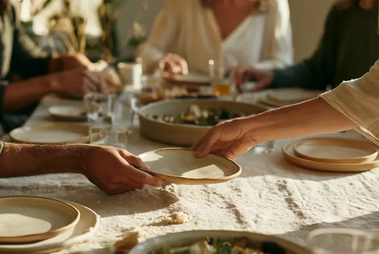 Dos personas se pasan un plato alrededor de una mesa mientras comparten una comida con amigos.